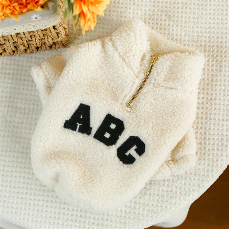 White dog fleece with 'ABC' text on a textured surface with flowers in the background