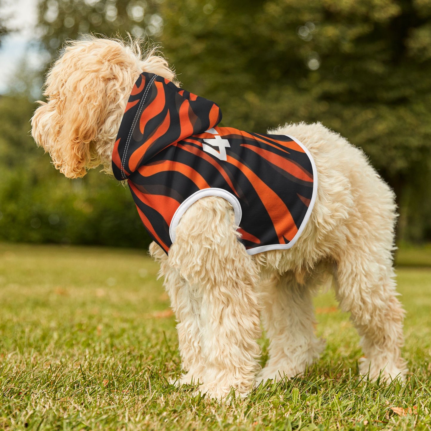 Dog wearing a black and orange striped hoodie with a white logo on grass