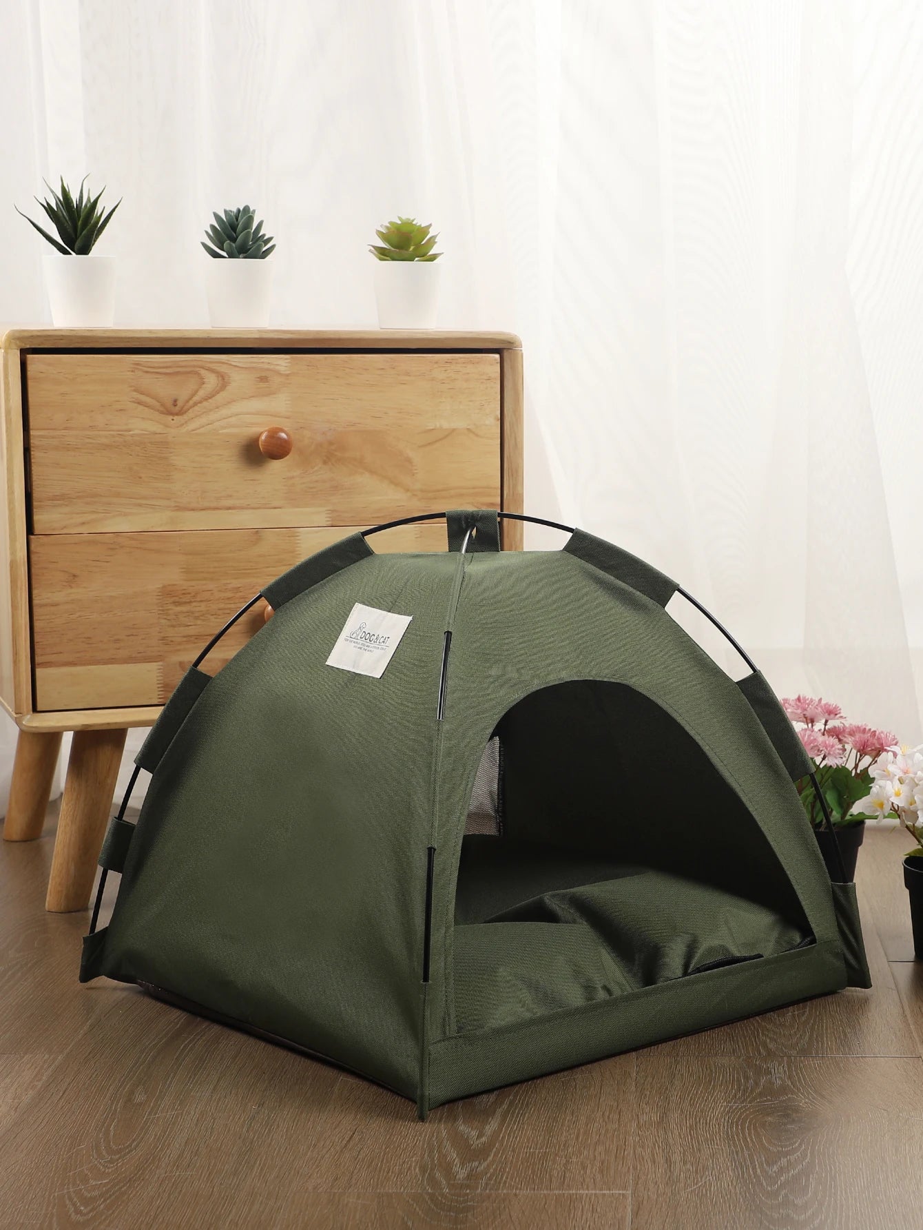 Green pet tent on a wooden floor with a wooden drawer and plants in the background
