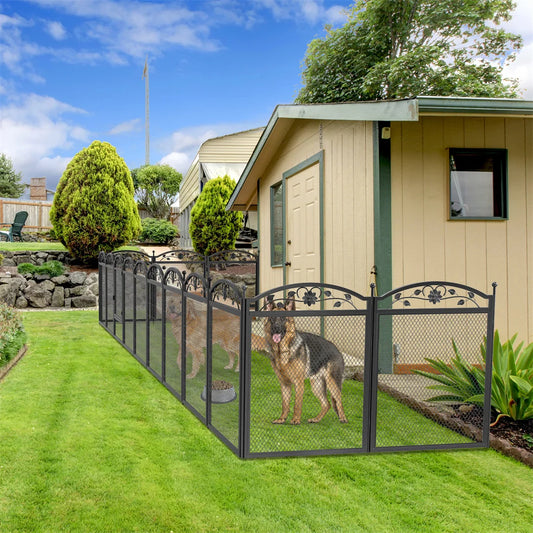 Dog standing behind a metal fence in a backyard with a house and garden in the background.