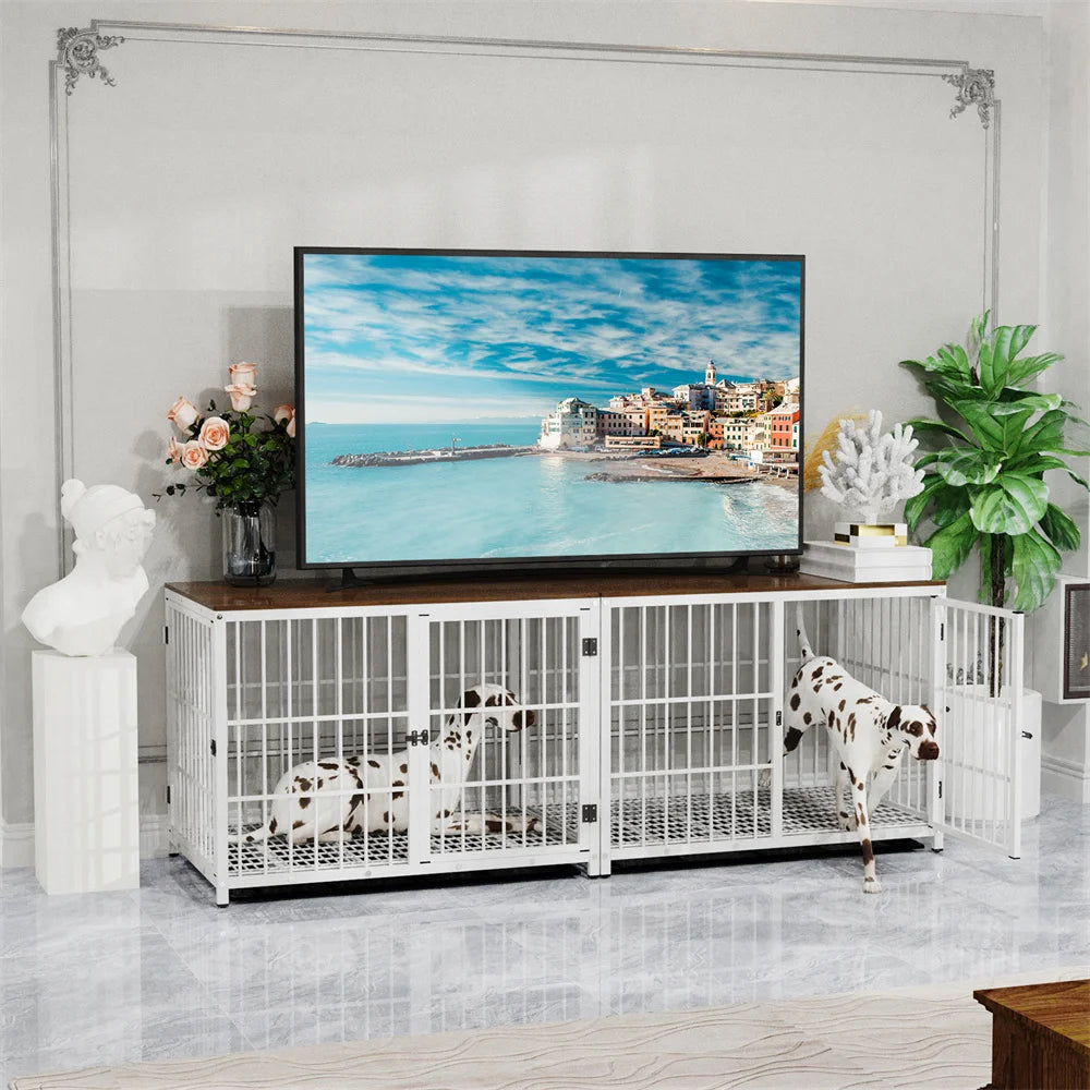 Two Dalmatian dogs in a white metal dog crate in a living room with a TV displaying a beach scene.