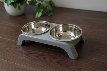 Two PawDine elevated pet bowl stands side by side on a wooden floor, one in black and one in grey