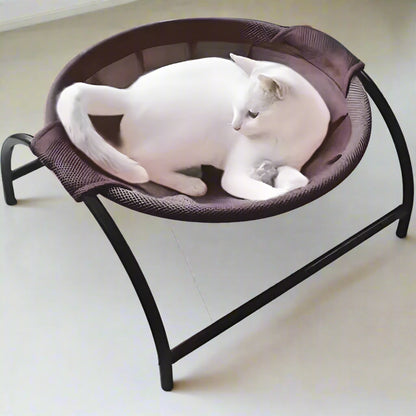White cat curled in the PawRest coffee brown mesh cat hammock bed, seen from above, on an arched black steel frame