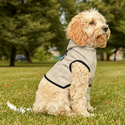 Dog wearing a gray quilted coat sitting on grass with trees in the background