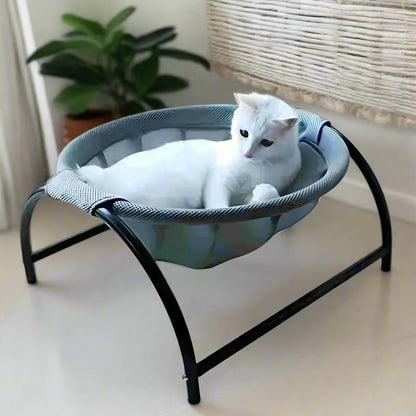 White cat lying in the PawRest grey mesh cat hammock bed in a bright room with window light and white floor tiles