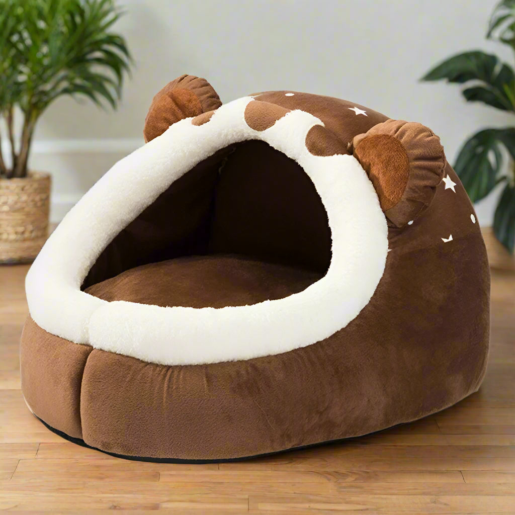 Small white dog sitting inside brown bear cave dog bed with 3D ears