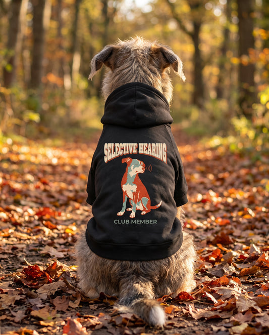 Dog sitting on an autumn path wearing the black Selective Hearing Club Member Dog Hoodie, back view