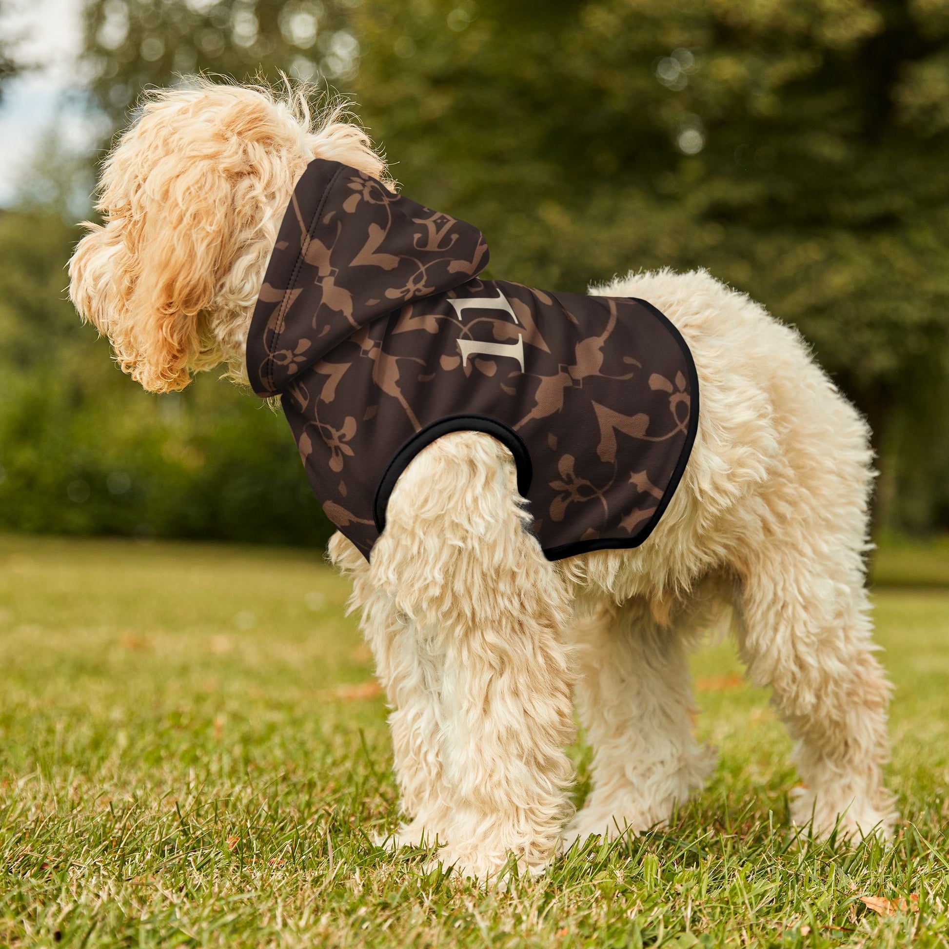 Dog wearing a black patterned raincoat on grass with trees in the background
