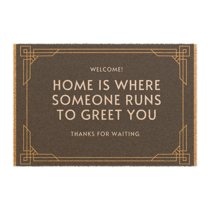 A rectangular doormat with the text 'WELCOME! HOME IS WHERE SOMEONE RUNS TO GREET YOU THANKS FOR WAITING' printed in black and gold colors.