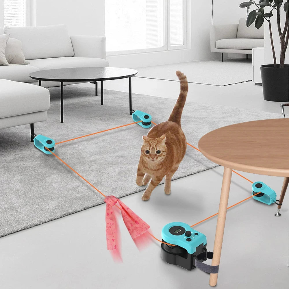 An interactive cat toy wheel exerciser with adjustable speed. The toy is set up in a room with a cat walking towards it, and it features a series of blue and green wheels connected by an orange ribbon to a cat collar.