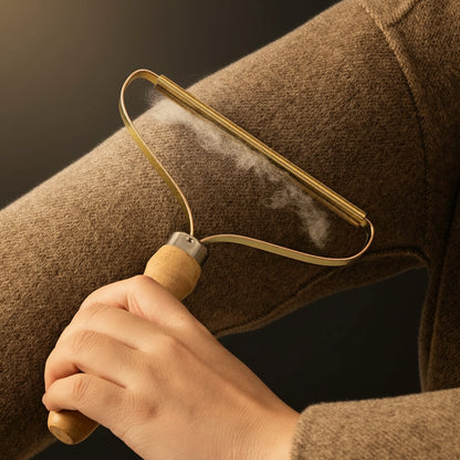 Wooden-handle fabric pet hair shaver with brass-coloured metal coil head, on a neutral pale-grey background, soft daylight.