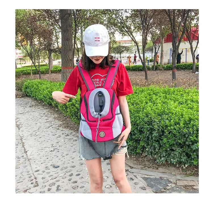 Person wearing a pink and gray pet carrier backpack outdoors.