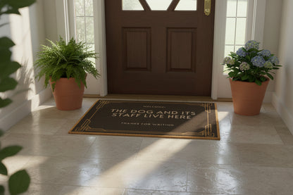 A brown doormat with the text 'WELCOME THE DOG AND ITS STAFF LIVE HERE THANKS FOR WAITING' printed on it.